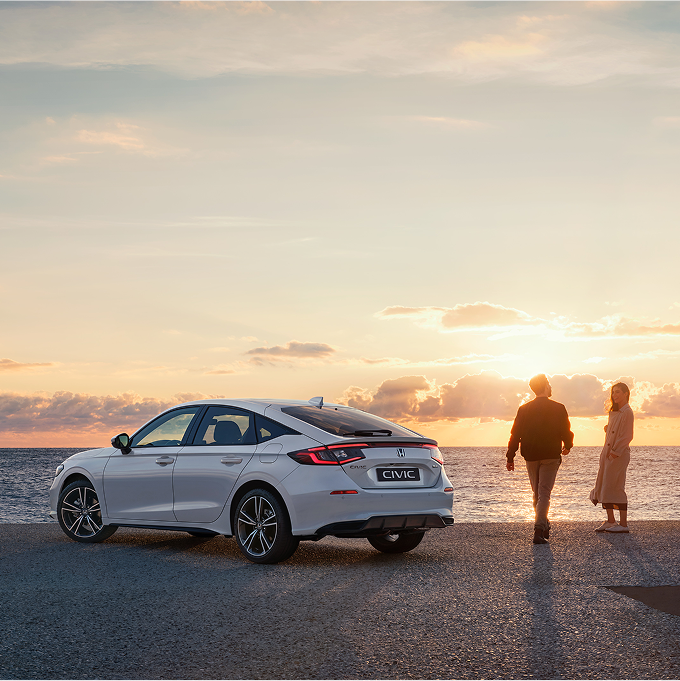 Honda Civic Hybrid zaparkovaná pri mori, ľudia stojaci na pravej strane auta.